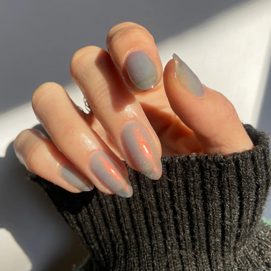 Close-up of a hand with light-colored nail polish wearing a dark textured sleeve.